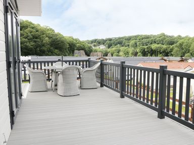 An outdoor balcony with four wicker chairs around a round table overlooking rooftops and trees at 44 Heritage Park Stepaside near Kilgetty