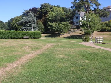 A grassy park area with trees benches paths and white houses in the background at Little Starboard in Kingsbridge