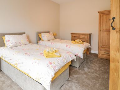 A bedroom with two single beds with floral bedding and yellow towels on them a wooden chest of drawers and a wooden wardrobe at Y Stabl in Llanddoged near Llanrwst