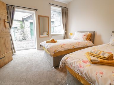 A bedroom with two single beds with floral bedding and folded towels near a window and wooden door at Y Stabl in Llanddoged near Llanrwst