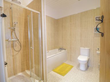 A bathroom with a shower enclosure bathtub toilet and yellow bath mat at Y Stabl in Llanddoged near Llanrwst