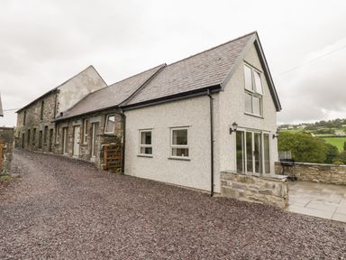 A gravel driveway leading to a stone and stucco house with a slate roof and patio at Y Stabl in Llanddoged near Llanrwst