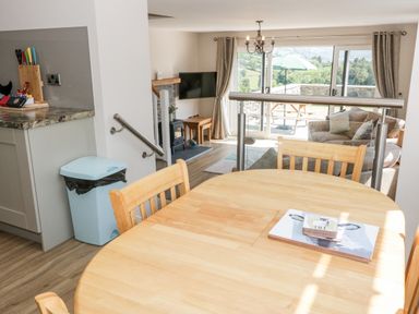 A dining area with a wooden table and chairs overlooking a living room with a sofa and a TV at Y Stabl in Llanddoged near Llanrwst