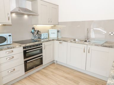 A kitchen with light-colored cabinets a double oven a sink a microwave and kitchen utensils at Y Stabl in Llanddoged near Llanrwst