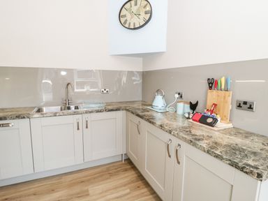 A kitchen corner with cabinets a sink a countertop with a kettle knife block and a clock on the wall at Y Stabl in Llanddoged near Llanrwst