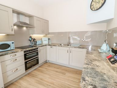 A kitchen with gray cabinets a double oven a sink a kettle and a microwave at Y Stabl in Llanddoged near Llanrwst