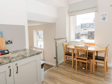 A dining area with a wooden table and four chairs next to a window in a kitchen at Y Stabl in Llanddoged near Llanrwst