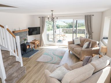 A living room with two sofas a fireplace a wall-mounted TV and sliding glass doors leading outside at Y Stabl in Llanddoged near Llanrwst