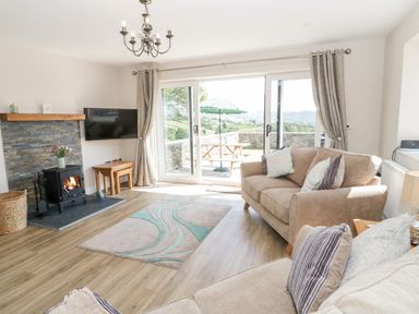A living room with sofas a rug a wood burning stove and sliding doors leading to a patio at Y Stabl in Llanddoged near Llanrwst