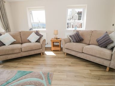 A living room with two beige sofas with cushions and a wooden side table with a lamp between them at Y Stabl in Llanddoged near Llanrwst