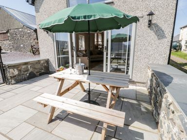 A patio with a wooden picnic table and benches under a green umbrella beside a stone wall at Y Stabl in Llanddoged near Llanrwst