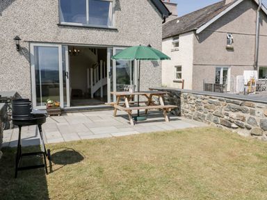 A backyard patio with a wooden picnic table and umbrella and a barbecue grill at Y Stabl in Llanddoged near Llanrwst