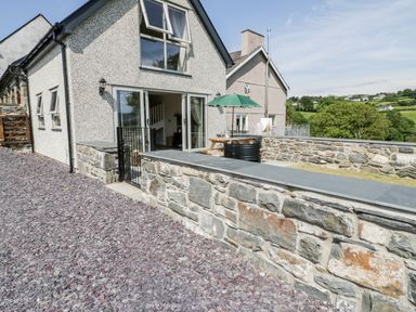 The outside of a house with a stone wall patio and a green umbrella over a wooden picnic table at Y Stabl in Llanddoged near Llanrwst