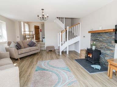 A living room with sofas a rug a fireplace stairs and dining table at Y Stabl in Llanddoged near Llanrwst