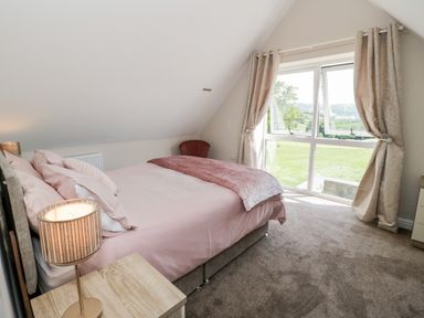 A bedroom with a bed bedside table lamp curtains and a window showing a green field at Y Stabl in Llanddoged near Llanrwst