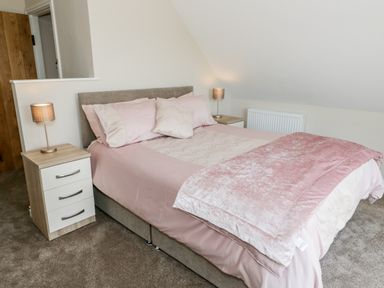 A bedroom with a double bed pink bedding and two bedside tables with lamps at Y Stabl in Llanddoged near Llanrwst
