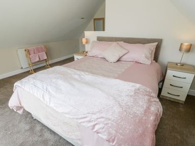 A bedroom with a pink bedspread pillows two bedside tables with lamps and a towel rack at Y Stabl in Llanddoged near Llanrwst