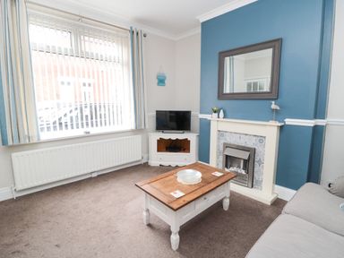 A living room with a wooden coffee table a fireplace with a mirror above and a TV on a corner unit at Sandy Toes Cottage in Newbiggin-By-The-Sea