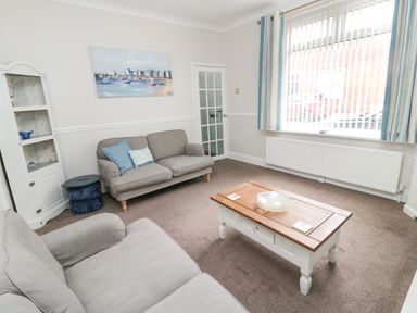 A living room with two sofas a wooden coffee table and a display cabinet at Sandy Toes Cottage in Newbiggin-By-The-Sea