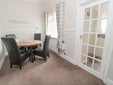 A dining area with a round wooden table and four black chairs beside a window with plaid curtains at Sandy Toes Cottage in Newbiggin-By-The-Sea