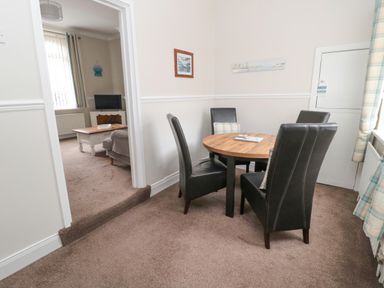 A dining area with a round wooden table and four black chairs near a window at Sandy Toes Cottage in Newbiggin-By-The-Sea