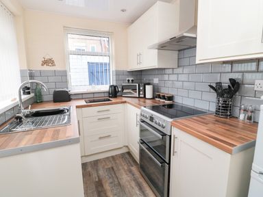 A kitchen with wooden countertops white cabinets a stainless steel oven a microwave and a window with blinds at Sandy Toes Cottage in Newbiggin-By-The-Sea