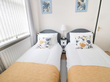 A bedroom with two single beds with white bedding and yellow throws at Sandy Toes Cottage in Newbiggin-By-The-Sea