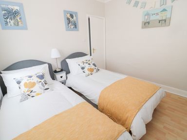 A bedroom with two single beds with pillows and blankets a small bedside table with a lamp and framed pictures on the wall at Sandy Toes Cottage in Newbiggin-By-The-Sea