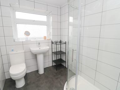 A bathroom with a toilet sink corner shelf and shower at Sandy Toes Cottage in Newbiggin-By-The-Sea