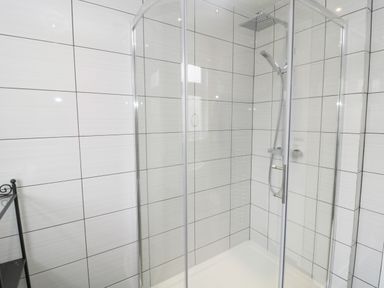 A shower enclosure with glass doors and tiled walls at Sandy Toes Cottage in Newbiggin-By-The-Sea