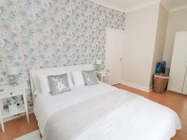 A bedroom with a double bed two bedside tables and lamps floral wallpaper and a wardrobe at Sandy Toes Cottage in Newbiggin-By-The-Sea
