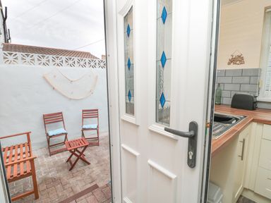 A kitchen with a sink toaster and tiled backsplash opening to a small patio with wooden chairs and a table at Sandy Toes Cottage in Newbiggin-By-The-Sea
