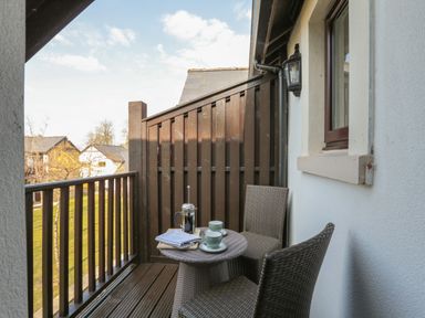 A small balcony with two wicker chairs a round wicker table with two cups a pot and folded cloths at Honeybee Cottage in Berrier near Penruddock