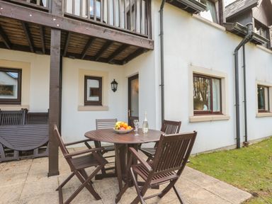 An outdoor patio area with a wooden table and four chairs and fruit bowl at Honeybee Cottage in Berrier near Penruddock