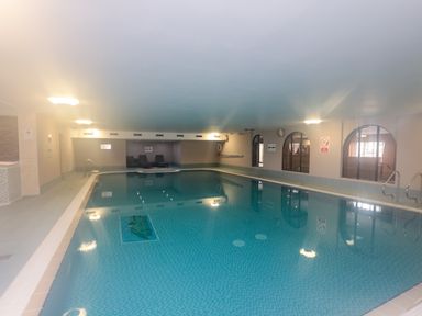 An indoor swimming pool with tiled floor and walls and lounge chairs at Honeybee Cottage in Berrier near Penruddock