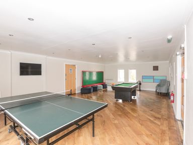 A game room with a ping pong table, billiards table, wall-mounted TV, seating area, and wooden floor at Honeybee Cottage in Berrier near Penruddock