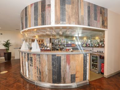 A curved bar counter with wood paneling and hanging glasses at Honeybee Cottage in Berrier near Penruddock