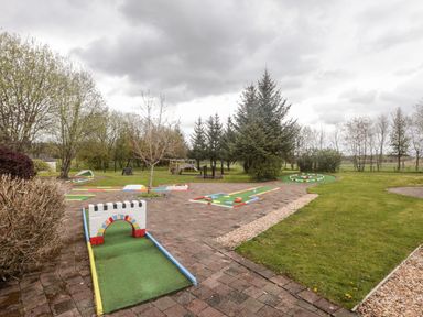 An outdoor mini golf course with various putting holes and green areas surrounded by trees at Honeybee Cottage in Berrier near Penruddock
