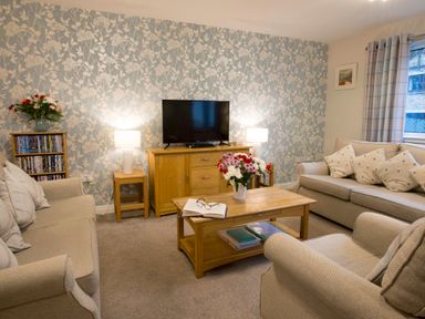 A living room with two sofas armchair wooden coffee table and TV unit at Honeybee Cottage in Berrier near Penruddock