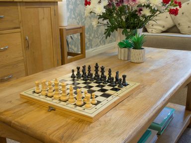 A chessboard with pieces set up on a wooden table with flowers and plants nearby at Honeybee Cottage in Berrier near Penruddock