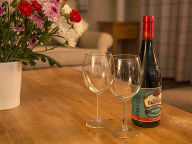 A wooden table with two empty wine glasses a bottle of red wine and a vase with flowers in a living room at Honeybee Cottage Berrier near Penruddock