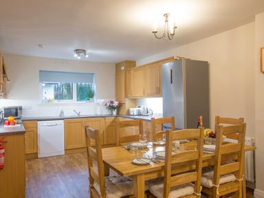 A kitchen with wooden cabinets a refrigerator a dining table with six chairs set with plates glasses and cutlery at Honeybee Cottage in Berrier near Penruddock