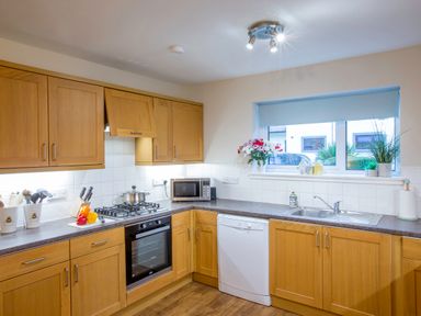 A kitchen with wooden cabinets a gas stove microwave dishwasher sink and window at Honeybee Cottage in Berrier near Penruddock