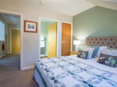 A bedroom with a bed with patterned bedspread pillows a bedside table with a lamp and doors leading to a hallway and bathroom at Honeybee Cottage in Berrier near Penruddock