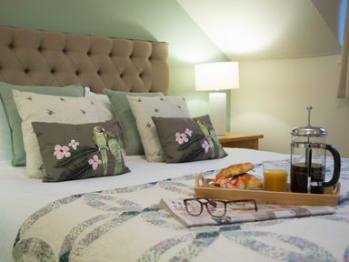 A bed with decorative pillows and a breakfast tray with coffee croissants orange juice and glasses at Honeybee Cottage in Berrier near Penruddock