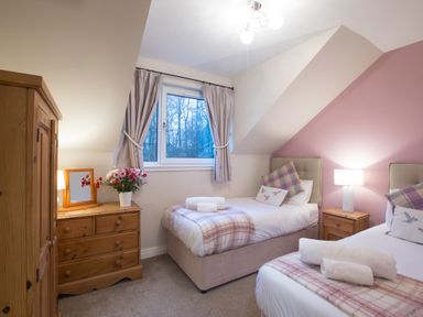 A bedroom with two single beds wooden furniture and a window with curtains at Honeybee Cottage in Berrier near Penruddock