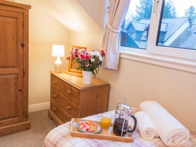 A bedroom corner with wooden dresser and wardrobe a window and breakfast on bed at Honeybee Cottage Berrier near Penruddock