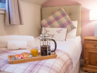 A bedroom with a bed that has pillows and a wooden tray with coffee juice and croissant at Honeybee Cottage in Berrier near Penruddock