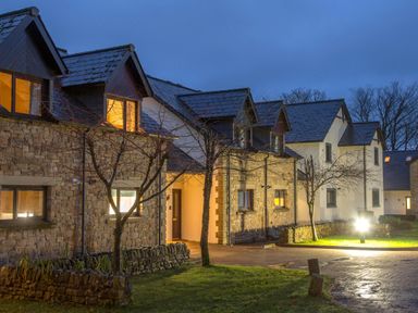 Stone and white houses with lit windows at dusk with trees and grass at Honeybee Cottage in Berrier near Penruddock