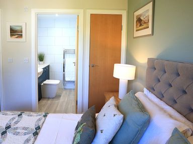 A bedroom with a bed and bathroom door at Honeybee Cottage in Penruddock
